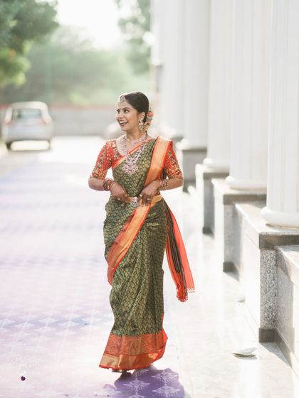 A candid shot of a bride walking with a smile, showcasing her beautiful green and orange wedding saree.