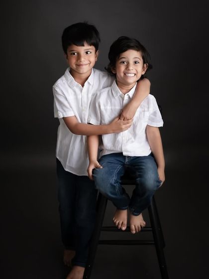 A classic portrait of two brothers. The simple setup with a stool allows their genuine smiles and brotherly affection to be the main story.