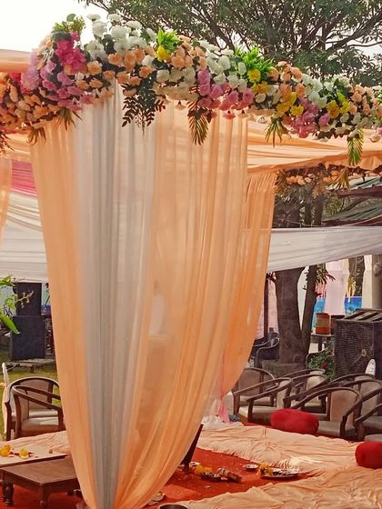 A simple and elegant mandap with peach and white fabric draping and a floral border, set up for a daytime garden wedding.
