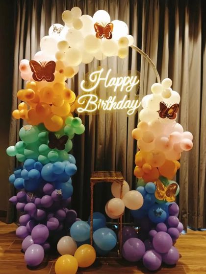 A rainbow-colored circular balloon arch decorated with butterflies. This cheerful and vibrant piece is perfect for a happy, colorful celebration.
