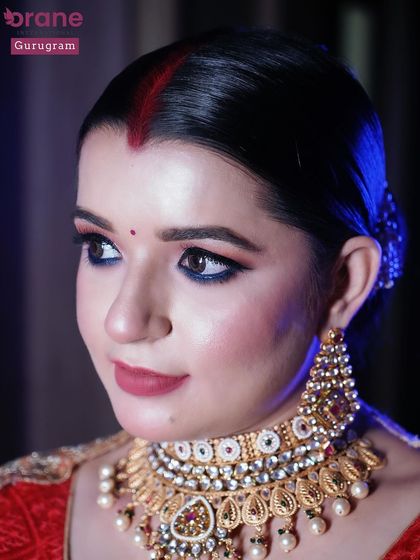 A classic reception makeup look with a red outfit and gold jewelry. The winged eyeliner and sindoor add a traditional touch to the glamorous style.