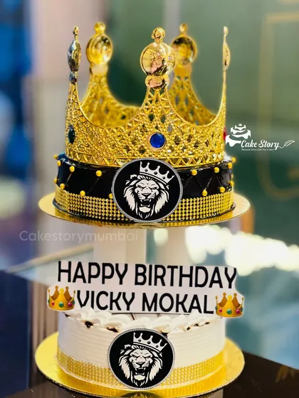 A royal two-tier 'King' theme cake. The top tier is adorned with a large, ornate golden crown, making it a majestic centerpiece for a birthday celebration.