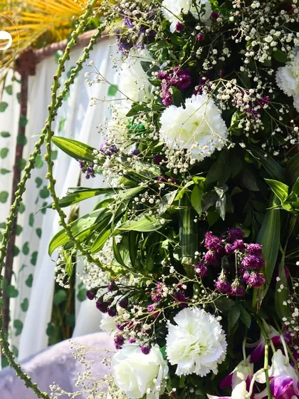 A close-up of a floral garland on a Roka mandap, showing the intricate weaving of white carnations, purple statice, and fresh greenery.