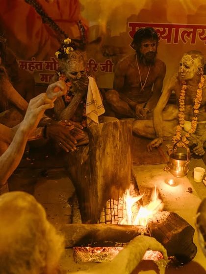 A group of Naga sadhus gathered around a sacred fire (dhuni) at night during the Kumbh Mela. The firelight creates a warm, communal, and deeply spiritual atmosphere.