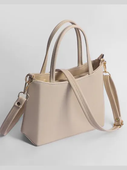 A beige handbag with its crossbody strap attached, photographed from the side to show its full profile.