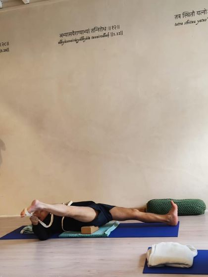 A supine leg and hip stretch using a strap, focusing on opening the outer hip.