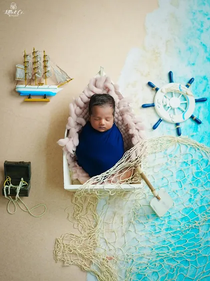 An overhead view of our popular sailor-themed newborn shoot. This angle showcases the full setup, from the sandy-colored base to the ocean-blue fabric, with carefully placed props like a miniature ship and treasure.