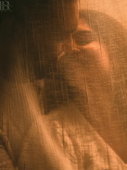 An artistic shot of a couple's embrace through a textured curtain, creating a moody, intimate, and mysterious portrait.