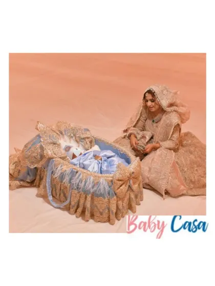 A dreamy welcome for a newborn. A mother in a beautiful traditional outfit sits beside her baby, who is resting in an ornate custom bassinet, creating a magical and memorable scene.