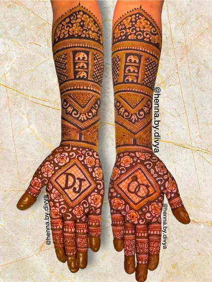 A full-arm engagement design with personalized initials 'DJ' and an engagement ring symbol. The arms are covered in traditional patterns, including elephant motifs and floral bands.