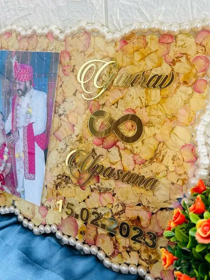 A 9x12 inch resin frame with a pearl border and a background of preserved light-colored rose petals. The design includes a wedding photo, names, and date.
