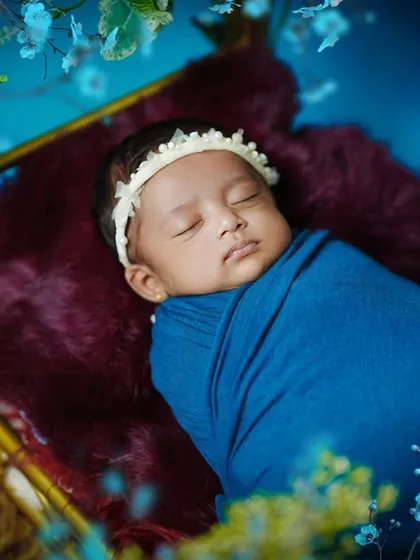A sleeping newborn rests in a miniature bed, surrounded by a magical blue floral arrangement. This setup creates a fairytale-like scene for your baby's first portraits.