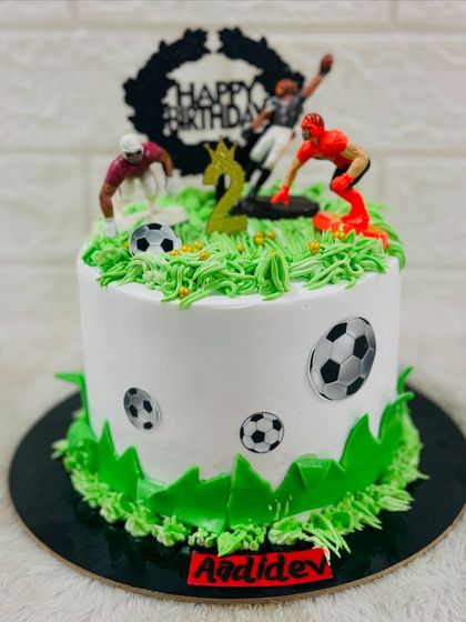 A fun football-themed cake for a 2nd birthday, with green buttercream "grass" and miniature players in action on top.