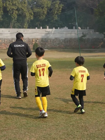 A coach leads his team onto the field. This image represents our commitment to expert coaching and long-term player growth, nurturing bright futures on and off the pitch.