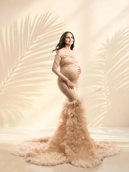 A full-length view of a stunning beige gown with a long, feathery train. The soft, warm lighting and shadow overlays give this studio portrait a gentle and dreamy quality.