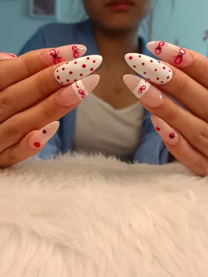 A playful and cute design with red polka dots and hand-drawn red bows on long almond nails.