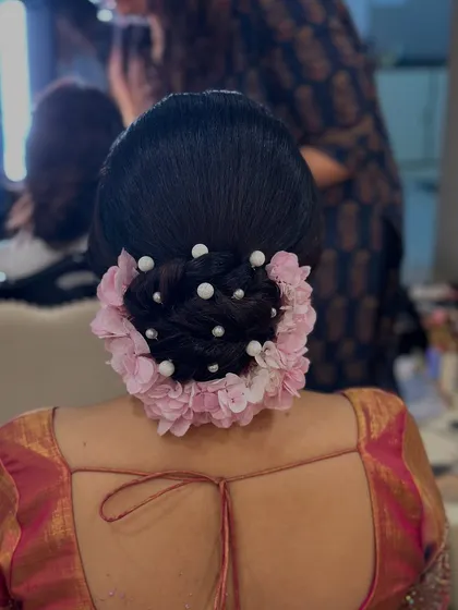 A close-up of the pink floral and pearl bun, showing the detail of the pearl pins scattered within the braided bun.