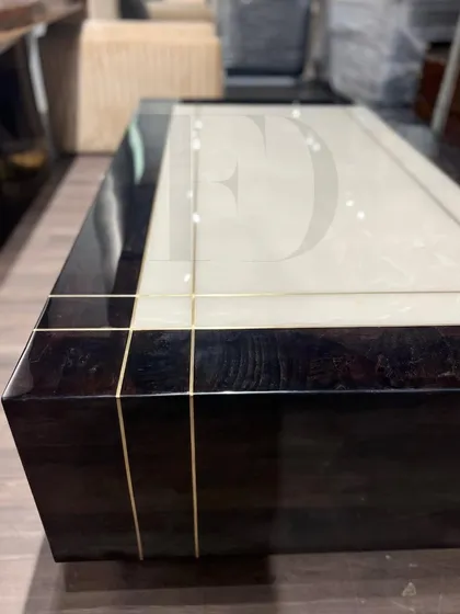 This center table combines a dark, high-gloss veneer with a central white onyx panel and delicate brass inlay. The design is a perfect example of modern luxury, blending different materials for a sophisticated result.