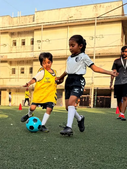 A girl skillfully dribbles past a boy, showcasing her confidence and control during a mixed-gender practice game.