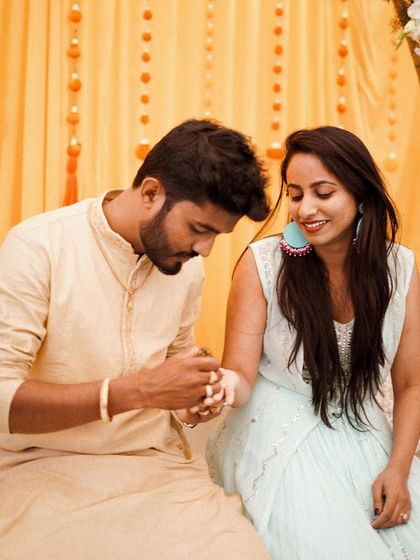 The groom applies henna to the bride's hand during the Mehendi ceremony. Our decor provides a beautiful and festive setting for these sweet traditions.
