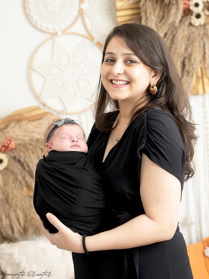 A beautiful portrait of a mother holding her sleeping newborn daughter. Her smile radiates pure joy and love in this warm, boho-inspired setting.