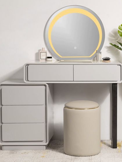 The Pure Precision vanity set features a minimalist design with clean lines and rounded corners. It includes a separate three-drawer unit for flexible placement, a round LED mirror, and a comfortable leather-topped pouf.