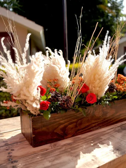 A wooden box centerpiece with pampas grass, pinecones, and pops of red. This arrangement is a great example of how I blend natural and rustic elements for a unique look.