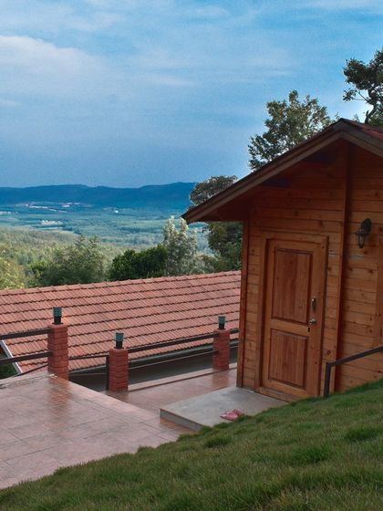 A wooden cabin perched on a hill in Chikmagalur, with a spacious terrace offering expansive views of the valley below.