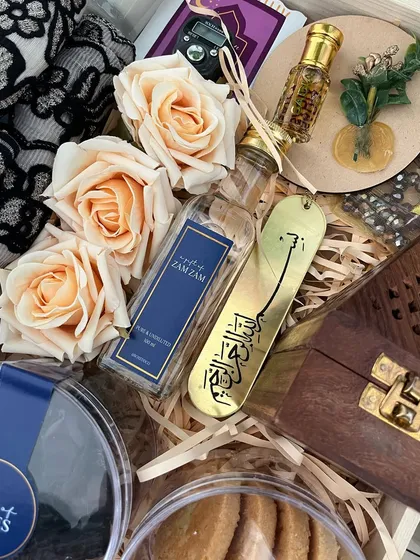 A close-up of the contents of a Ramadan hamper, including a bottle of Zamzam water, a golden Islamic bookmark, and a wooden box for Bakhoor.