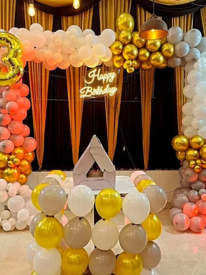 An elegant indoor birthday setup with a balloon arch in shades of peach, white, and gold.