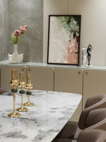 Every element in this dining console area is meticulously curated. The sleek cabinetry with a textured stone backdrop adds dimension, while decorative accents like abstract artwork and sculptural figurines introduce personality and depth.