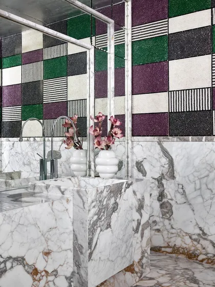 A powder room in the Ventura gallery that showcases a bold approach to materials. I contrasted the organic, heavy veins of the marble vanity with graphic, multi-patterned mosaic tiles on the wall. It's an example of how I use unexpected combinations to create visual interest and a sense of quiet luxury.