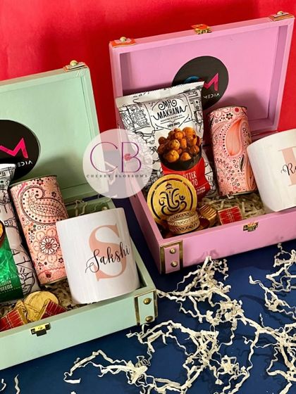 Our Diwali hampers are ready to delight your dear ones. This image shows our pastel-coloured leatherette trunks filled with snacks, a Ganesha T-light holder, and a personalised mug.