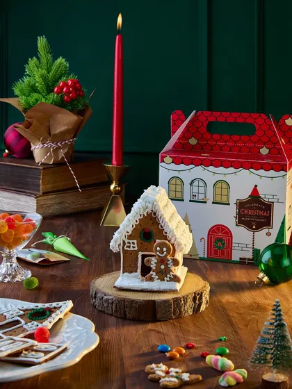 A whimsical shot focusing on a DIY gingerbread house from the Marriott Bonvoy Christmas collection. The warm, woody tones and festive decorations create a magical, storybook feel that appeals to families.