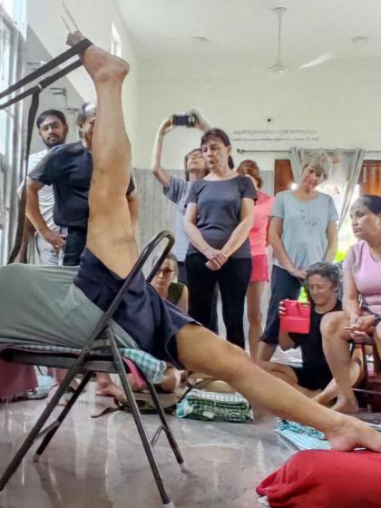 A supported leg stretch, similar to Supta Padangusthasana, demonstrated to an attentive class. The chair provides a stable base to work on hamstring flexibility.