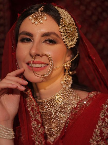A close-up portrait of a bride in a classic red outfit. Her hair is styled to accommodate the heavy passa and maang tikka, creating a look of timeless royal elegance.