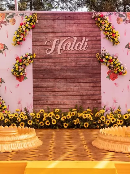 The main stage for a Haldi ceremony, featuring a rustic wooden backdrop adorned with sunflowers. This design combines natural elements with bright florals for a warm and inviting feel.