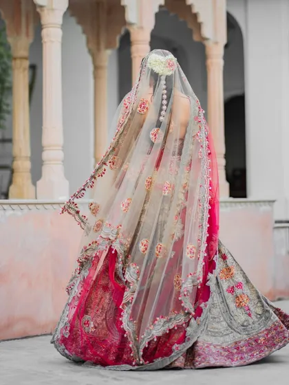 A back profile of the bride, focusing on the exquisite details of her embroidered veil and the floral arrangement in her hair. This shot emphasizes the artistry of the bridal attire.
