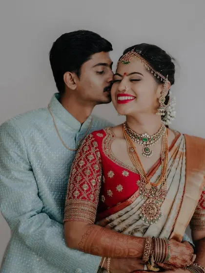 A candid couple shot where the bride wears a beautiful off-white and red Kanchipuram saree. Her red blouse features a unique quilted embroidery pattern.