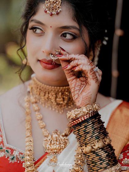 A delicate and artistic close-up of the bride adjusting her nose ring. This shot highlights the intricate details of her jewelry and henna.