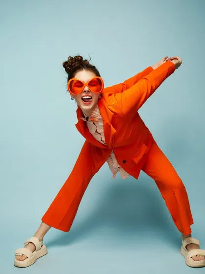 A fun, quirky, and colorful look with a bright orange suit and oversized sunglasses, showing our students' versatility.