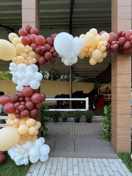 An organic balloon arch in earthy tones frames the entrance to the stables, creating a festive welcome for the horse-themed party.