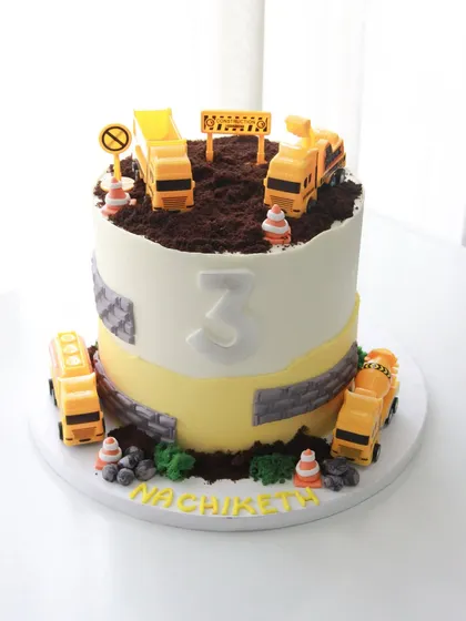 A construction zone cake for Nachiketh's 3rd birthday. This fun design features edible "mud" made from chocolate, toy trucks, and traffic cones for a playful and interactive cake.