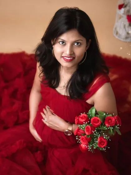 A unique top-down perspective of a mom-to-be in a gorgeous red gown, looking up at the camera. The gown spreads out around her like a flower, and she holds a bouquet of red roses, creating a romantic and creative shot.