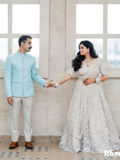 A clean and elegant portrait against a simple, bright background. The groom leading the bride by the hand creates a sense of a new journey beginning, with their coordinated pastel outfits adding to the soft aesthetic.