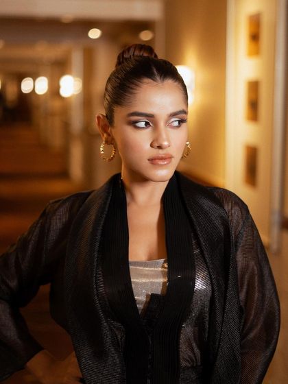 An elegant portrait in a warmly lit hallway. The soft lighting and the model's confident expression capture a moment of quiet glamour, highlighting the texture of the sheer jacket.