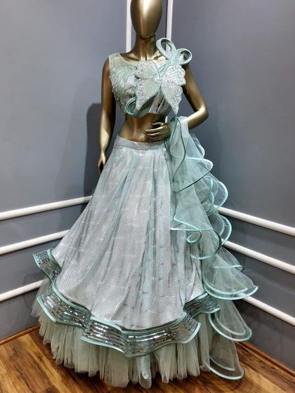 A modern ruffled lehenga in a pastel blue shade. The structured butterfly-style blouse and layered skirt make this a trendy and high-fashion choice for a cocktail party.