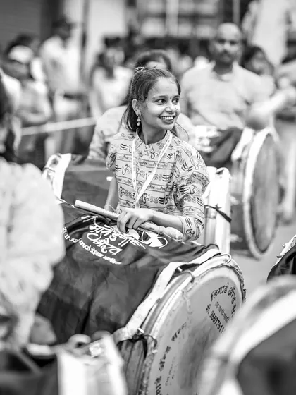 The black and white version of the smiling drummer, her joy shining through in this candid festival moment.