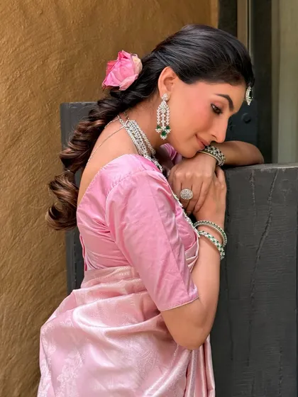 A beautiful side profile showing the romantic braided hairstyle adorned with a fresh pink rose. The makeup is soft and glowing, with a focus on flawless skin.