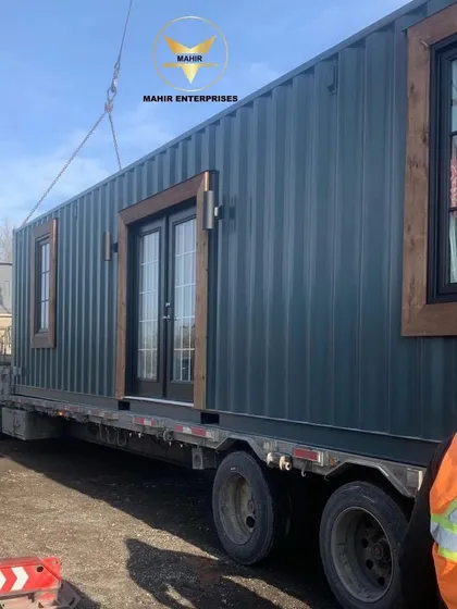 A finished container home, complete with custom windows and doors, securely placed on a flatbed truck. Our team manages the entire shipping process to ensure your new space arrives safely and on schedule.